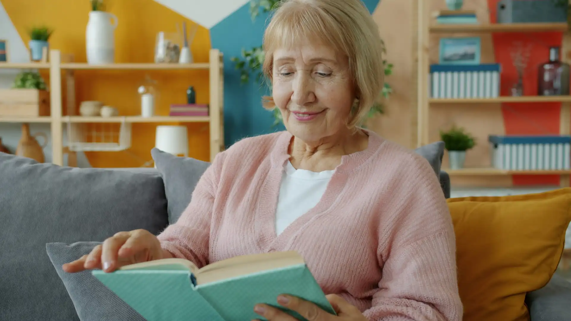 Mujer mayor leyendo un libro sin gafas en el sofá de su casa